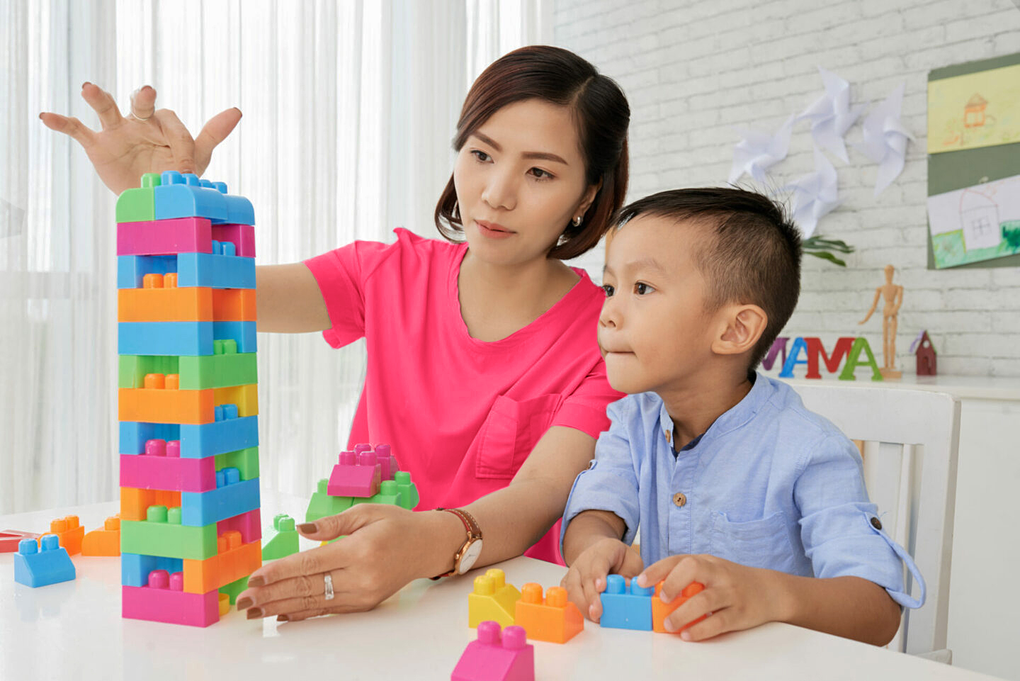 Nurse and pediatric patient building toy block towers in home.