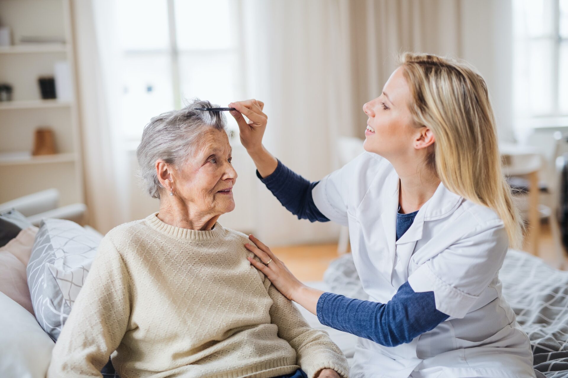 A health visitor combing hair of senior woman at home..