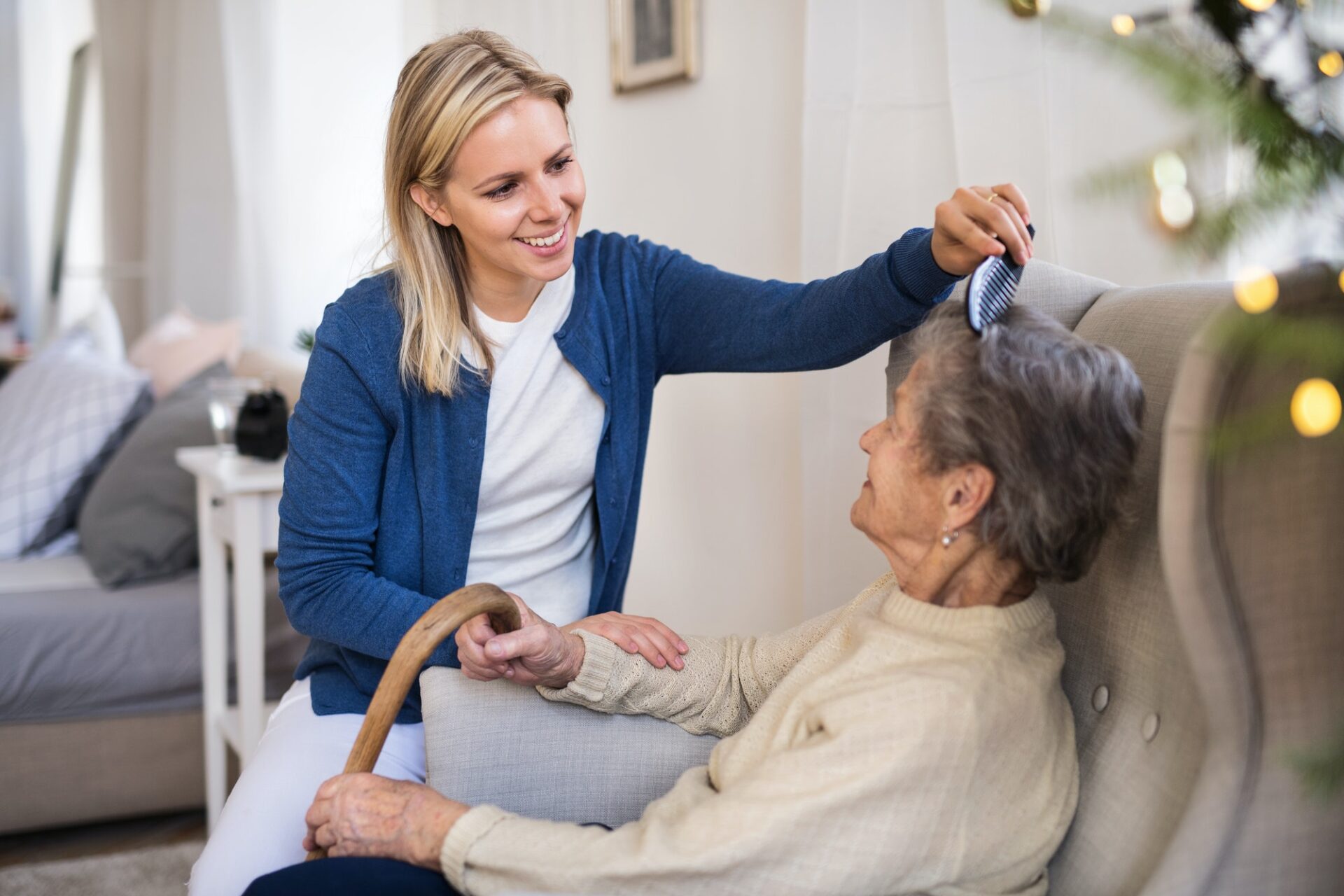 A health visitor combing hair of senior woman at home at Christmas time.