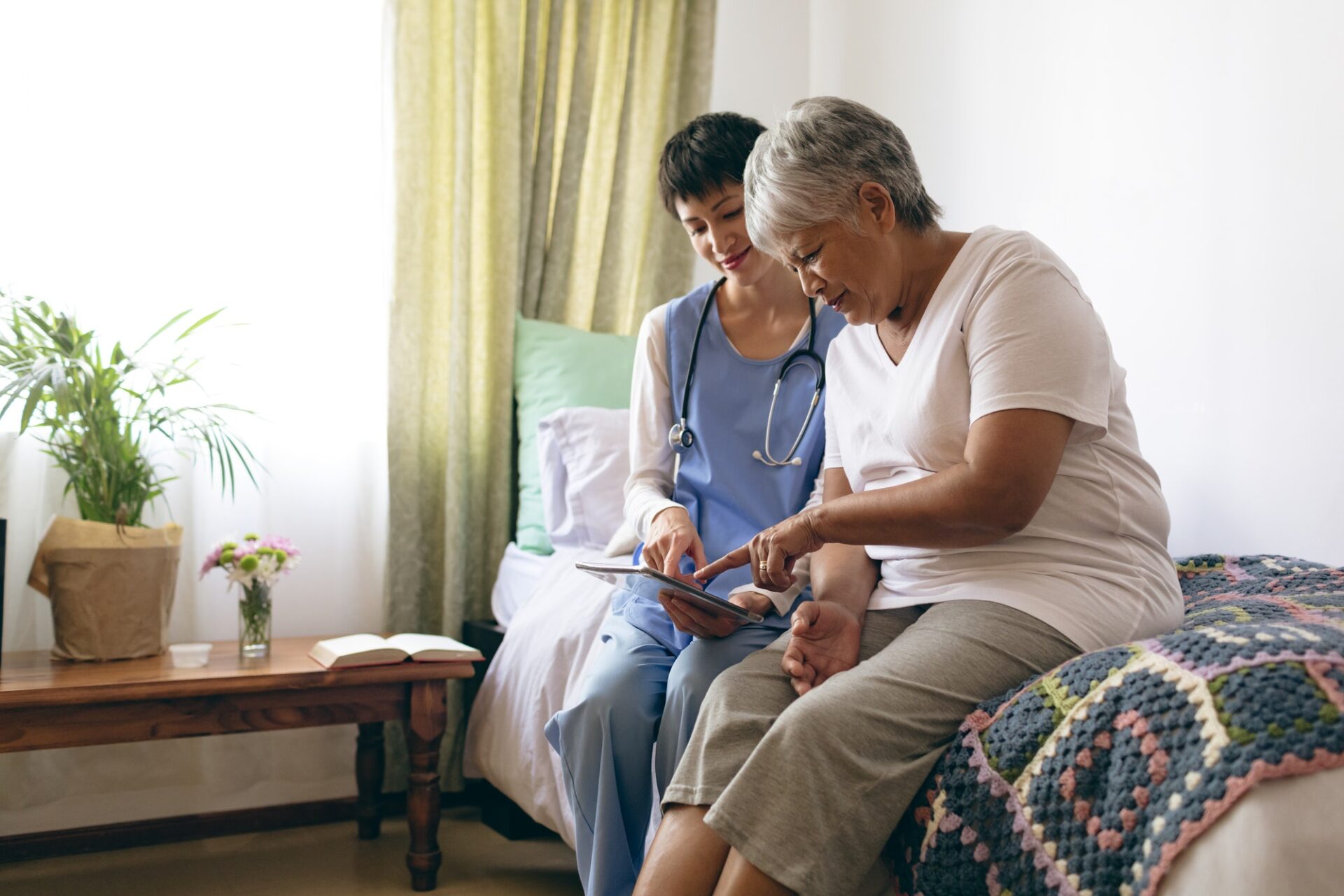 Beautiful female doctor and senior female patient using digital tablet at retirement home