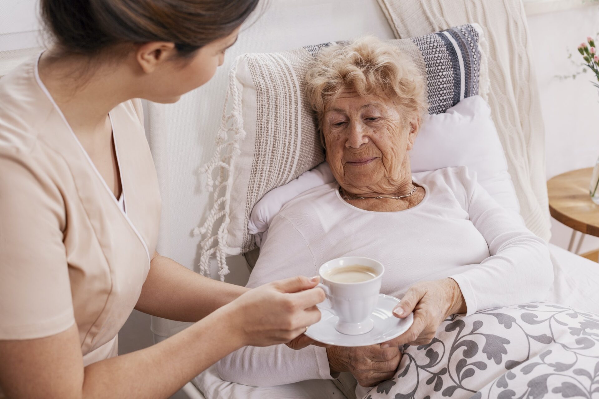 Beautiful young nurse serves tea to an elderly lady in a private nursing home