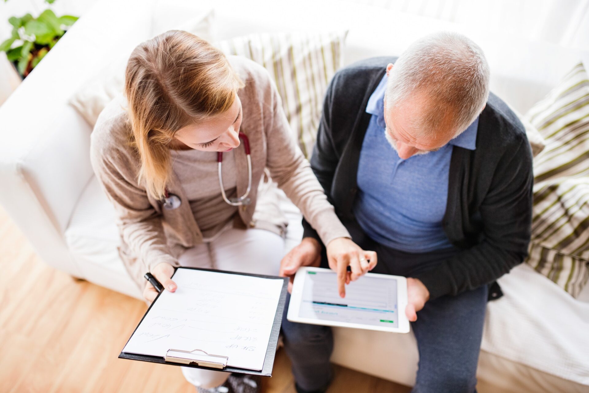 Health visitor and a senior man with tablet during home visit.