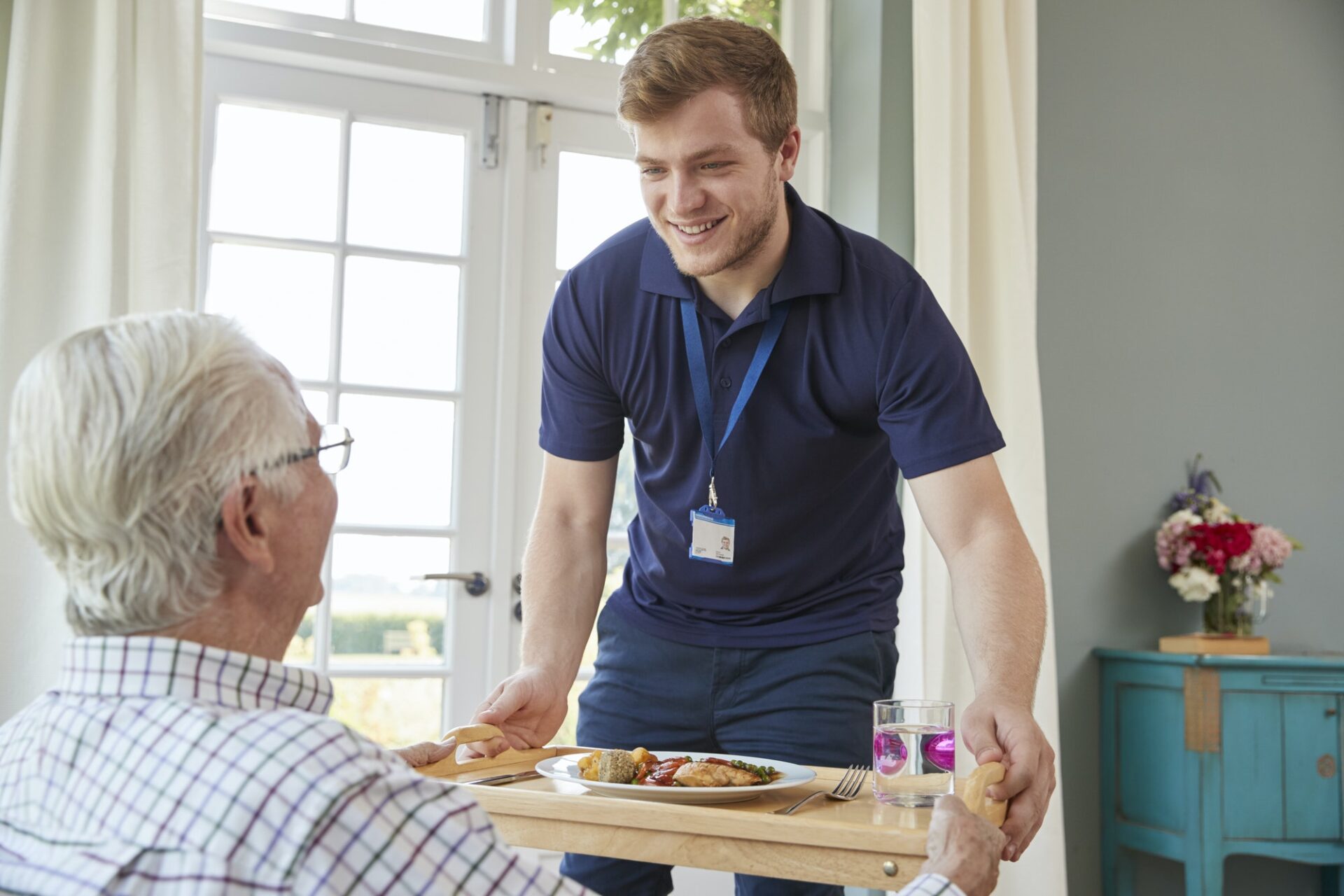 Male care worker serving dinner to a senior man at his home