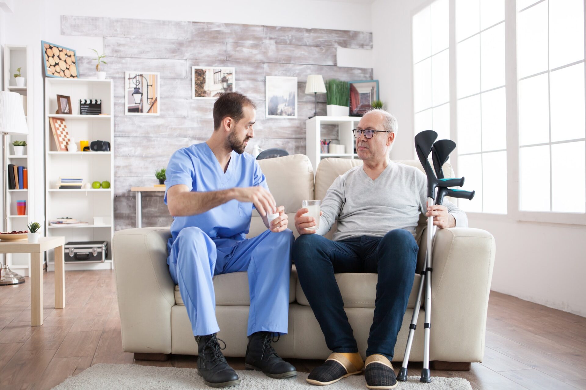 Young male nurse in nursing home with pills for senior man