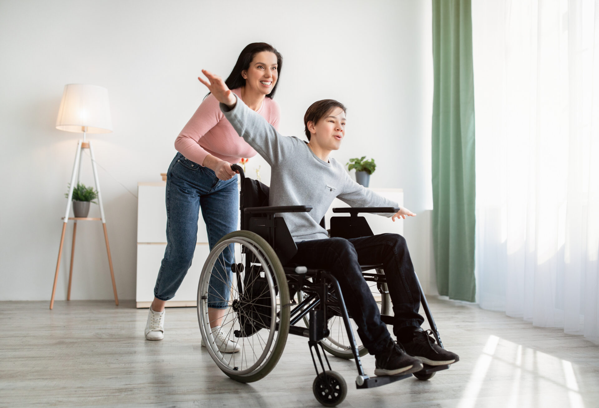 Young mother and her disabled son in wheelchair having fun, playing together at home.